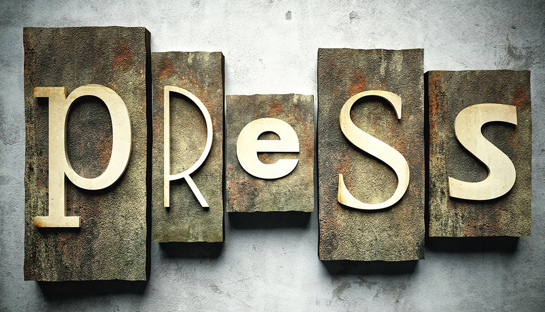 Das Bild zeigt 5 Steine und das englische Wort "press". Auf jedem Stein ist ein Kleinbuchstabe des Wortes "press" zu sehen. Die Steine liegen auf einem grau-weißen Beton-Hintergrund.