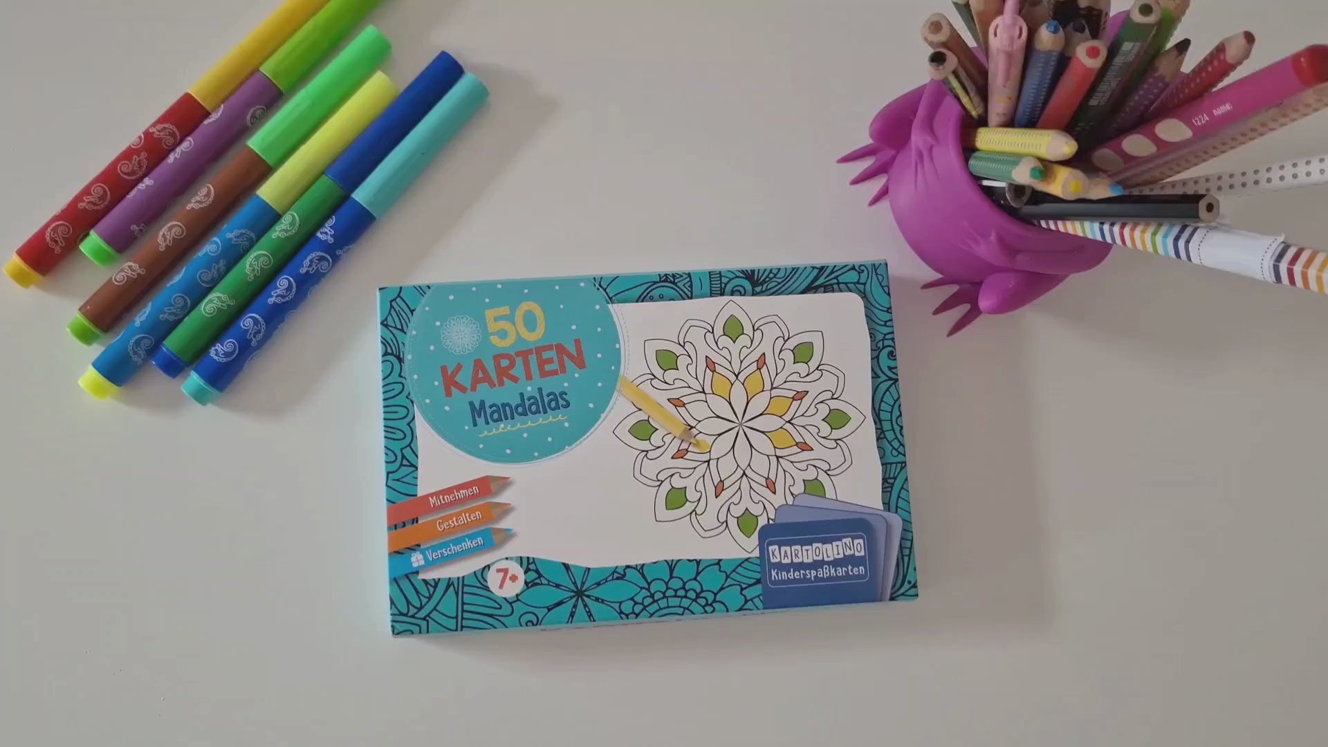 Laden Sie das Video: In diesem Video werden Aussehen und Funktionsweise der KARTOLINO Kartenbox "50 Karten zum Ausmalen -  Mandalas" gezeigt. Zudem welche Mandala-Motive enthalten sind und dass die Box sich aufgrund ihres handlichen Formats perfekt zum Mitnehmen eignet. Ein Kind demonstriert, wie und mit welchen Stiften die Karten ausgemalt werden und beschriftet eine Kartenrückseite. Entspannung und Kreativität werden beim Ausmalen gefördert.